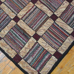 A close-up of a high-pile rug with beige, maroon, and multicolored striped diagonal checkerboard pattern on wood flooring.