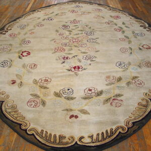 An oval rug on wood flooring features a cream field with scrolling red, pink, and green floral motifs and a complex dark border.
