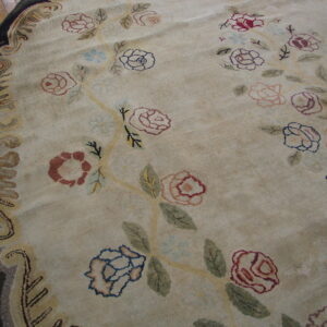 Round beige rug with scattered pink, blue, and red roses, bordered by dark scrollwork on wood.