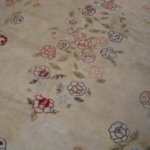 Low pile beige rug with an all-over design of large red, pink, and blue floral clusters.