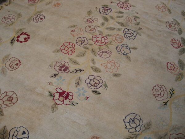 Low pile beige rug with an all-over design of large red, pink, and blue floral clusters.