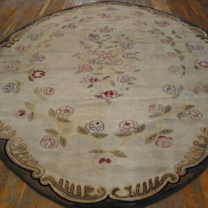 Oval cream rug with colorful roses and an ornate brown border rests on visible wood plank flooring.