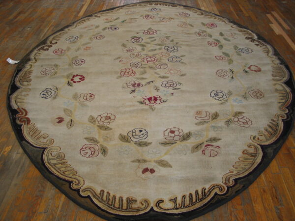 Oval cream rug with colorful roses and an ornate brown border rests on visible wood plank flooring.