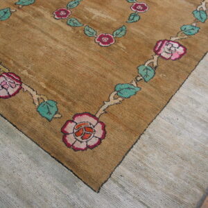 Close-up of a textured brown rug with a garland border of pink roses and teal leaves, resting on light flooring.