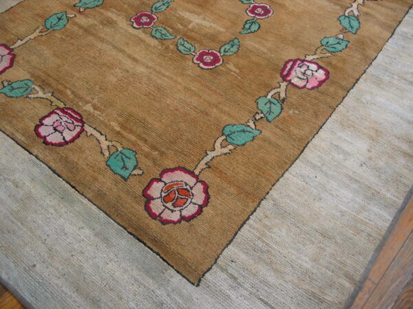 Close-up of a textured brown rug with a garland border of pink roses and teal leaves, resting on light flooring.