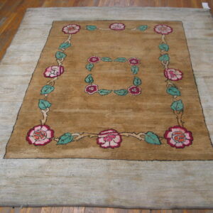 Large camel rug with gray outer border and pink floral squares rests on wood planks.