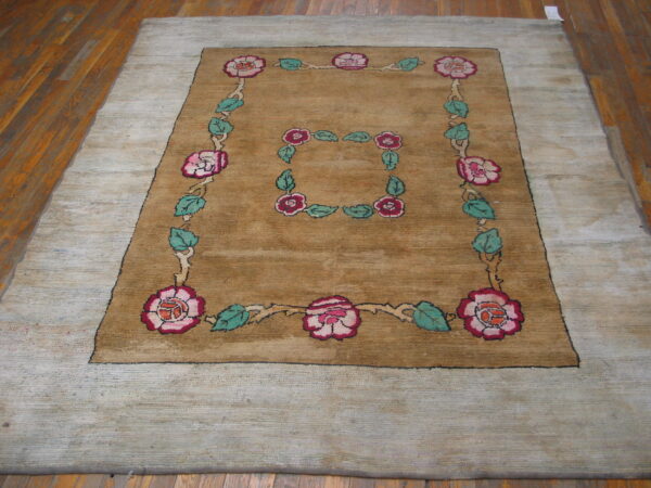 Large camel rug with gray outer border and pink floral squares rests on wood planks.