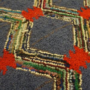 The high-pile blue rug features a zigzag pattern of colorful woven strips accented by red floral shapes.