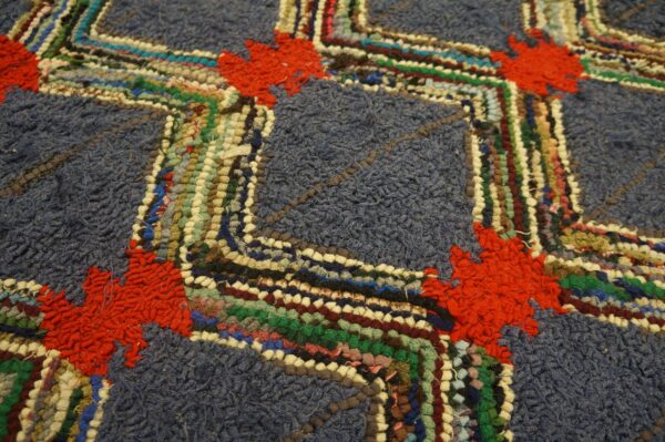 The high-pile blue rug features a zigzag pattern of colorful woven strips accented by red floral shapes.