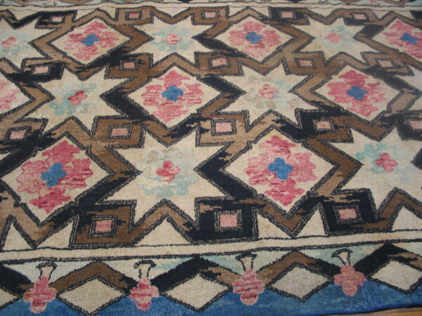 Geometric rug pattern featuring large cream stars outlined in black and brown surrounding pink and blue floral details.