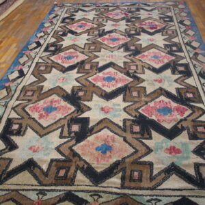 Geometric rug with cream field, black and brown outlines, pink and blue accents on wood flooring.