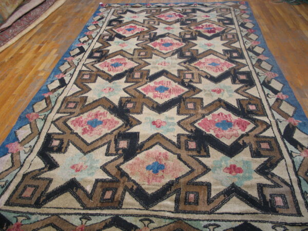 Geometric rug with cream field, black and brown outlines, pink and blue accents on wood flooring.