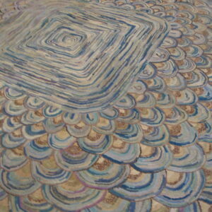 Textured rug with blue, tan, and brown overlapping scales surrounding a striped diamond center.