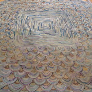 A round rug featuring a large blue, gray, and purple concentric square center surrounded by scalloped scales on wood floor.