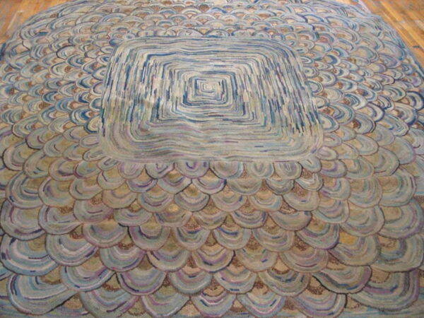 A round rug featuring a large blue, gray, and purple concentric square center surrounded by scalloped scales on wood floor.