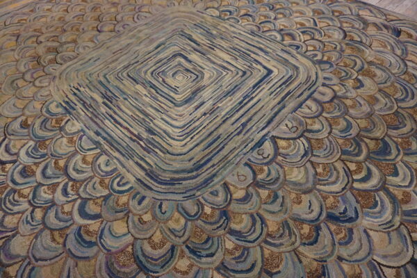 Textured rug showing a central diamond pattern surrounded by rows of blue and tan scallops.