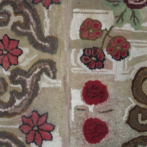 Highly textured rug detail features red florals and brown scrolls on a variegated beige and cream background.