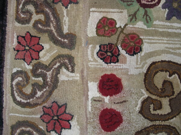 Highly textured rug detail features red florals and brown scrolls on a variegated beige and cream background.