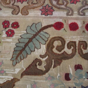 Close-up detail of a beige rug with plush pile and scrolling floral elements in brown, teal, and red.