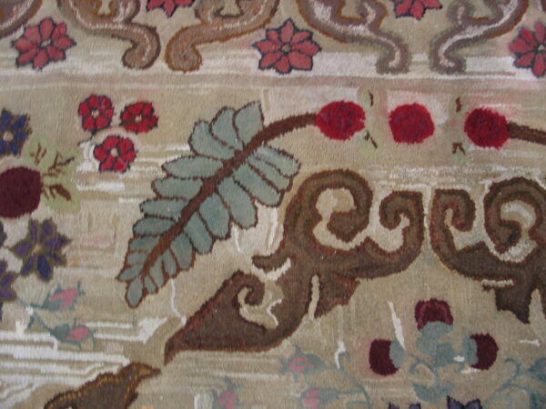 Close-up detail of a beige rug with plush pile and scrolling floral elements in brown, teal, and red.