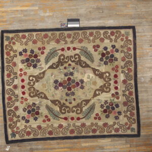 Beige, high-pile rug displaying an intricate floral medallion in burgundy, sage, and brown upon worn wood flooring.
