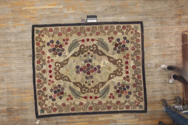 Beige, high-pile rug displaying an intricate floral medallion in burgundy, sage, and brown upon worn wood flooring.