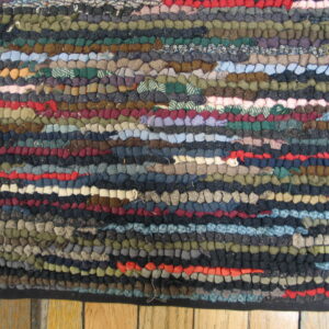 Close-up of a multi-colored hooked rag rug with dense texture and variegated horizontal rows resting on wood planks.