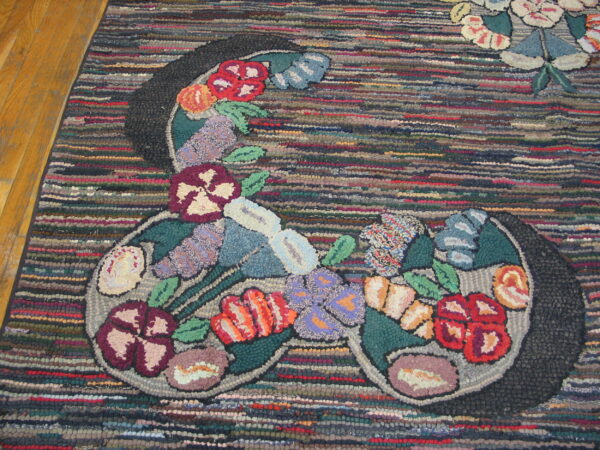 Chunky hooked rug with a central colorful floral design against a highly textured, striped background on wood floor.