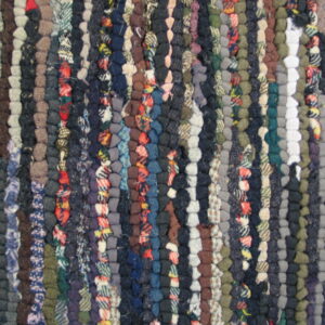 The rug features a dense braided texture with vertical stripes in navy, gray, brown, and red mixed colors.