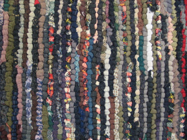 The rug features a dense braided texture with vertical stripes in navy, gray, brown, and red mixed colors.