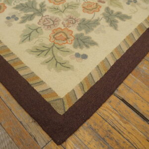 A low-pile cream rug with orange and green flowers and a thick brown border rests on worn wood flooring.