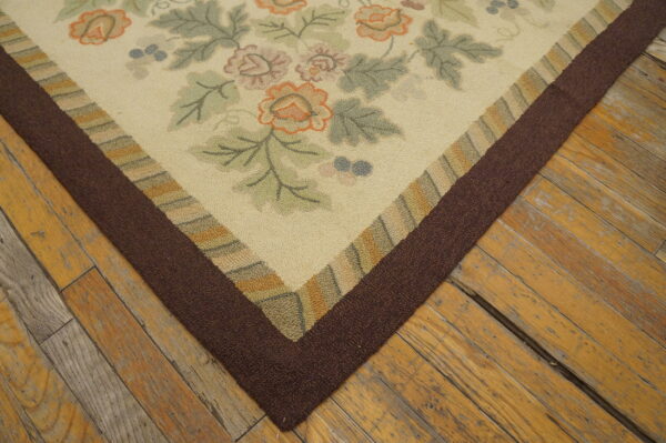 A low-pile cream rug with orange and green flowers and a thick brown border rests on worn wood flooring.