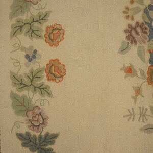 Muted floral hooked rug features a light beige field bordered by brown, green, orange, and blue motifs.