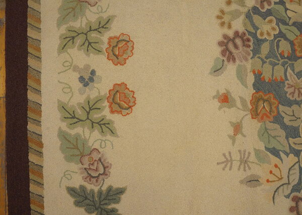 Muted floral hooked rug features a light beige field bordered by brown, green, orange, and blue motifs.
