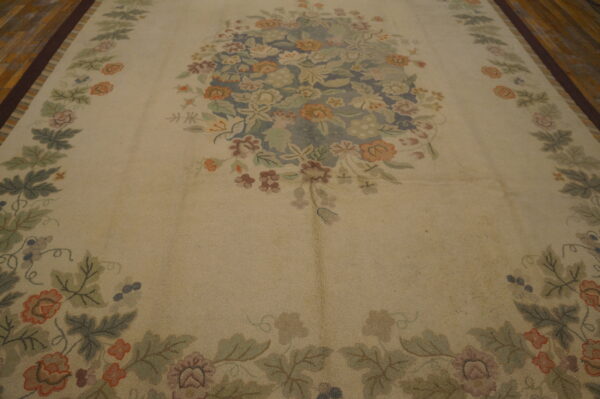 Beige rug with a detailed multicolored floral medallion and vine border on dark plank flooring.