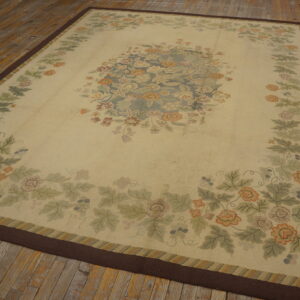 Ornate light beige floral rug featuring green, blue, and orange motifs, resting on distressed wood flooring.