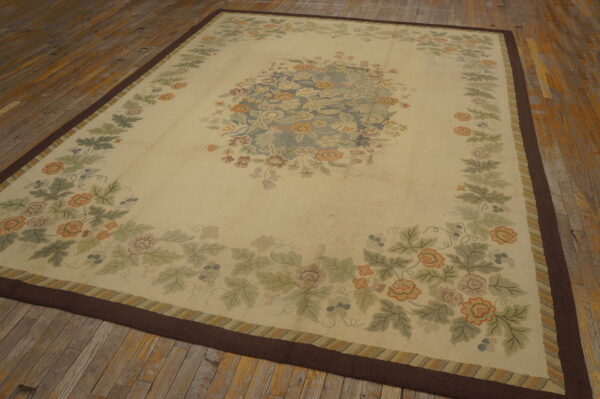 Ornate light beige floral rug featuring green, blue, and orange motifs, resting on distressed wood flooring.