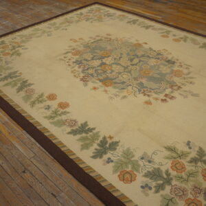 Cream rug with rust and sage floral patterns, dark border, lying on rustic plank wood flooring.
