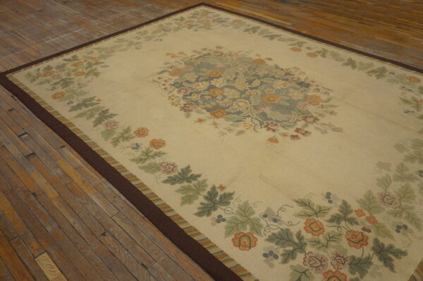 Cream rug with rust and sage floral patterns, dark border, lying on rustic plank wood flooring.