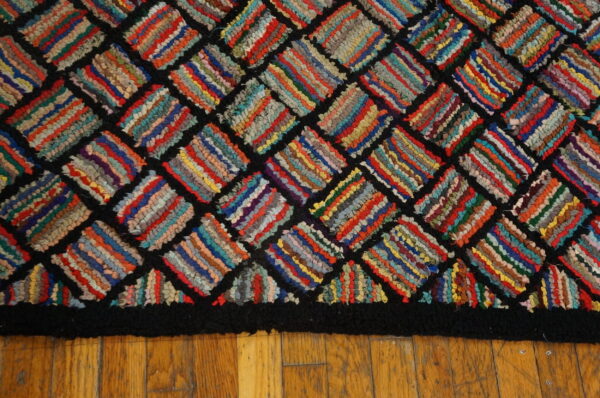 Multicolored hooked or braided rug with a black diamond lattice pattern and border on hardwood flooring.