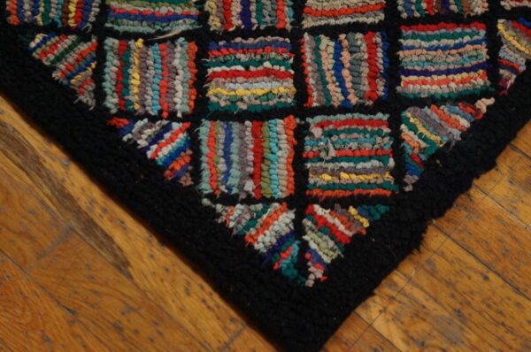 High-texture rag rug corner with colorful strip blocks and a thick black border on wooden floors.