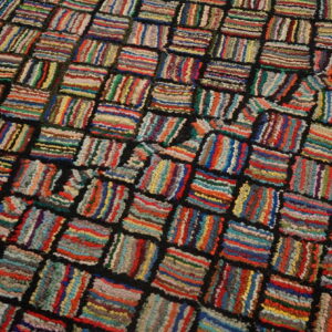 A shaggy, multicolored rug pattern of vibrant striped rectangles arranged in a dark grid structure.