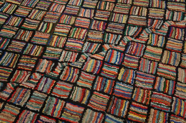 A shaggy, multicolored rug pattern of vibrant striped rectangles arranged in a dark grid structure.