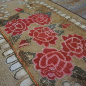 Tan looped rug with large pink rose florals, gray leaves, and a scalloped white border on distressed wood.