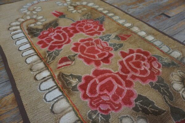 Tan looped rug with large pink rose florals, gray leaves, and a scalloped white border on distressed wood.
