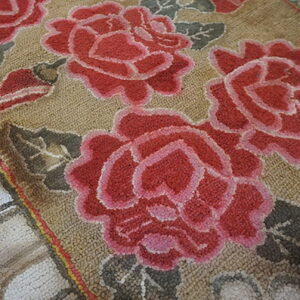 Textured tan rug featuring large red and pink roses with muted gray-green leaves.