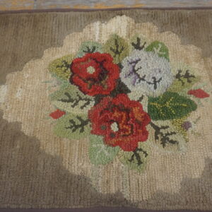 Hooked rug detail showing a red, white, and green floral cluster on a beige scalloped medallion and taupe field.