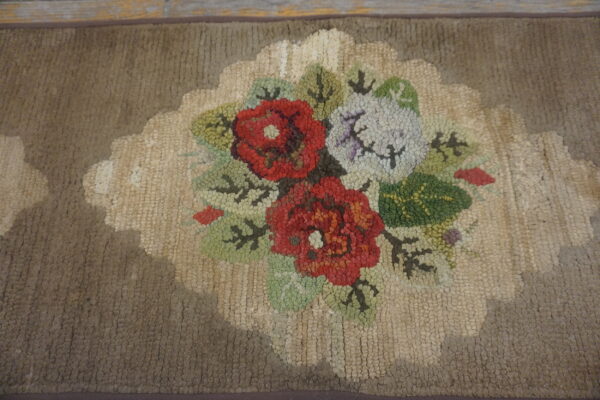 Hooked rug detail showing a red, white, and green floral cluster on a beige scalloped medallion and taupe field.