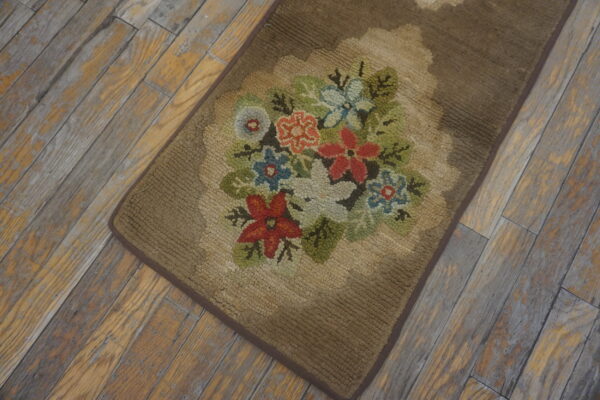 Brown hooked runner rug displaying a red, white, blue, and green floral bouquet on worn wood.