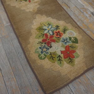 A tan looped runner rug with multicolored floral designs rests on distressed gray wood plank flooring.